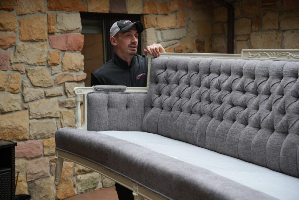 Person holding a tufted gray sofa.